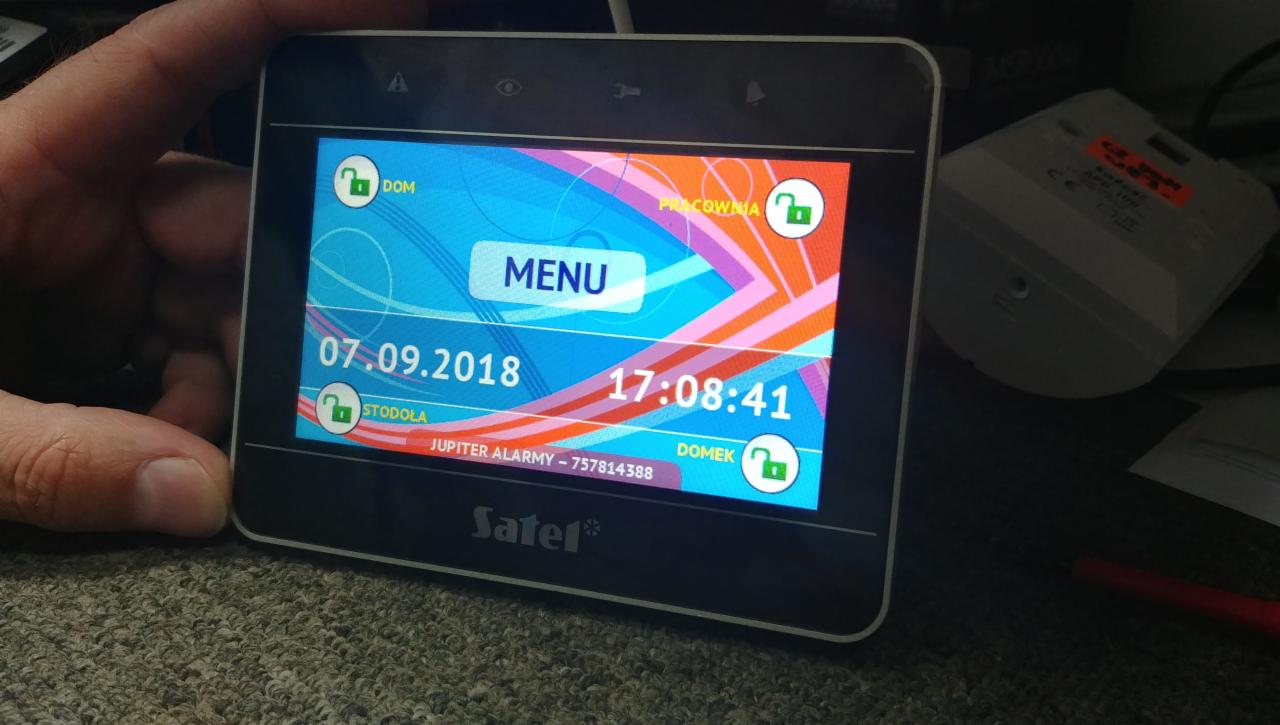 Ekran dotykowy centrali alarmowej Satel z widocznym menu i statusem zabezpieczeń poszczególnych stref: Dom, Stodoła, Pracownia, Domek. Na ekranie widoczna data 07.09.2018 i godzina 17:08:41.