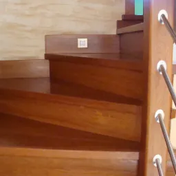 Drewniane schody spiralne z metalową balustradą, widok z dołu, ciepłe oświetlenie podkreśla usłojenie drewna.