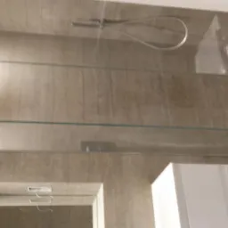 Wykończona łazienka z beżowymi płytkami, szklanymi półkami z podświetleniem LED i białym szafką pod umywalkę, widoczna armatura prysznicowa.