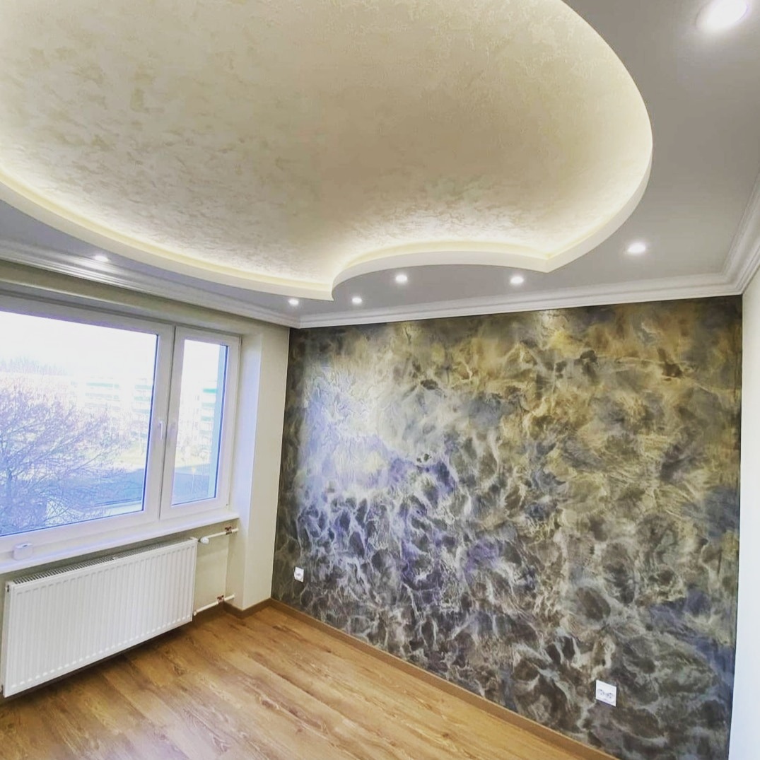 Pokój po remoncie z dekoracyjną ścianą w odcieniach szarości, brązu i fioletu, drewniana podłoga, okno z białymi ramami i grzejnikiem, sufit z podwieszaną konstrukcją i oświetleniem LED.