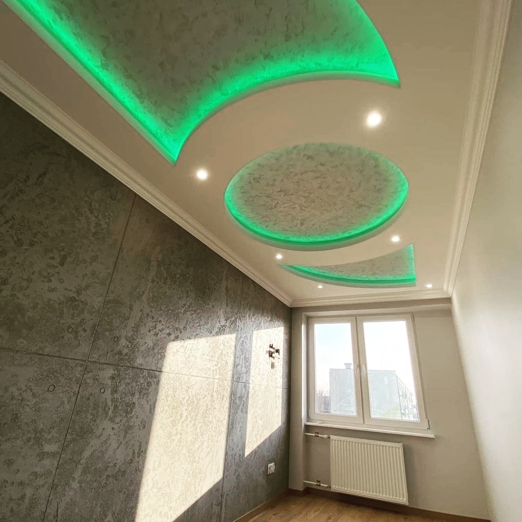 Pokój z dekoracyjnym, podwieszanym sufitem z zielonym oświetleniem LED, ściana z efektem betonu, okno z grzejnikiem.
