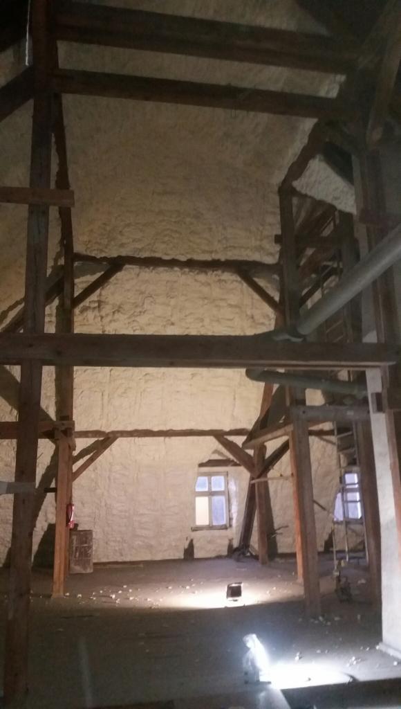 Poddasze w trakcie prac izolacyjnych we Wrocławiu, ściany i dach pokryte grubą warstwą jasnej piany, widoczne drewniane elementy konstrukcyjne i okno.