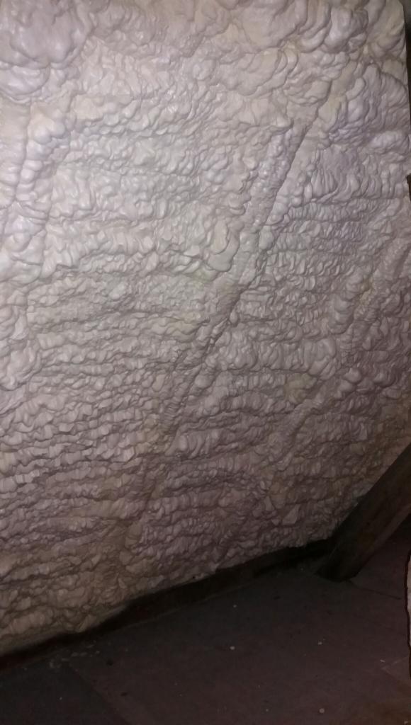 Szczegółowe ujęcie wewnętrznej strony dachu po nałożeniu warstwy izolacyjnej z pianki, widoczne nierówności i struktura materiału.