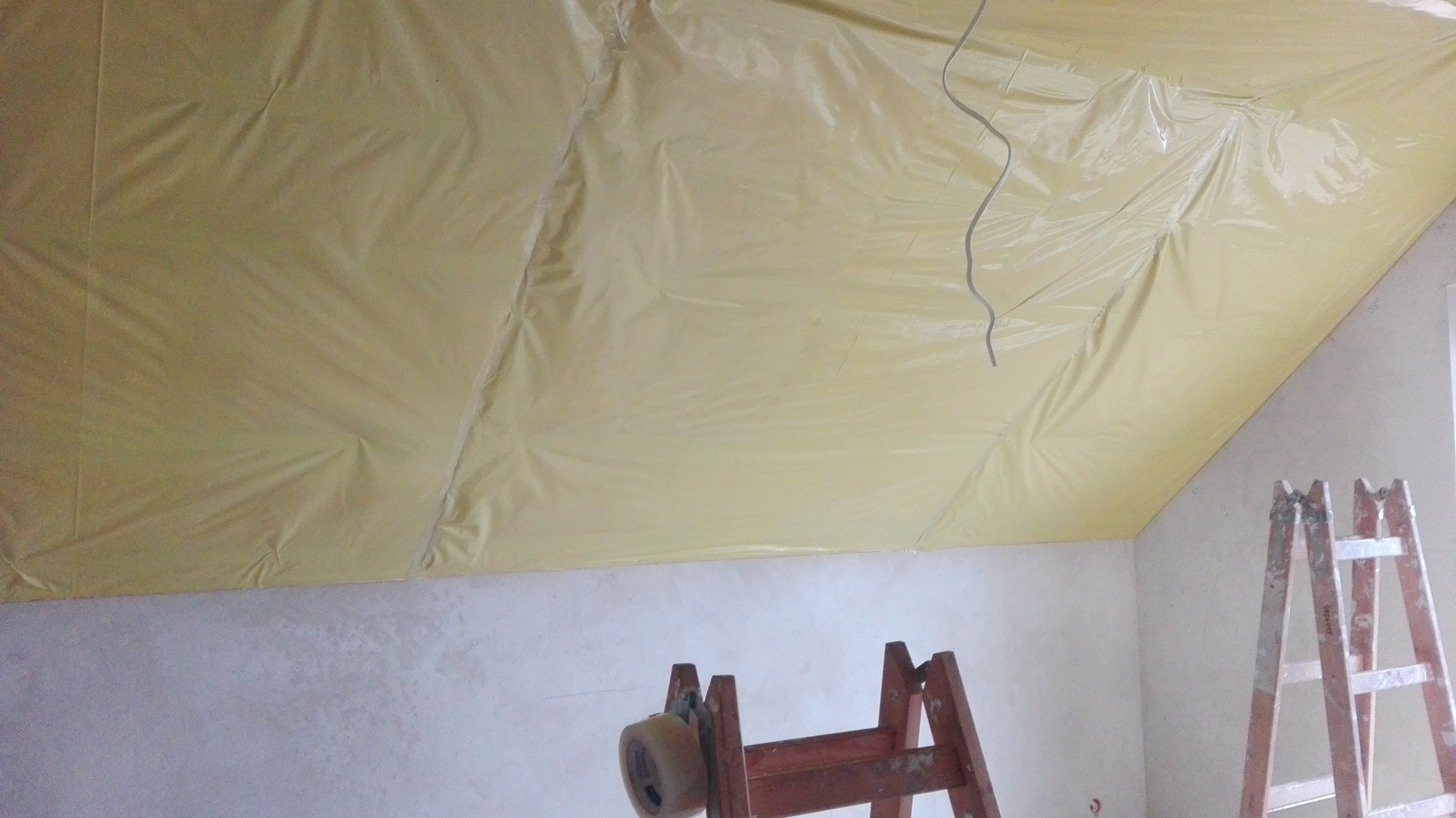 Przygotowanie poddasza do szpachlowania: folia ochronna na suficie skośnym, widoczne drabiny i taśma malarska.