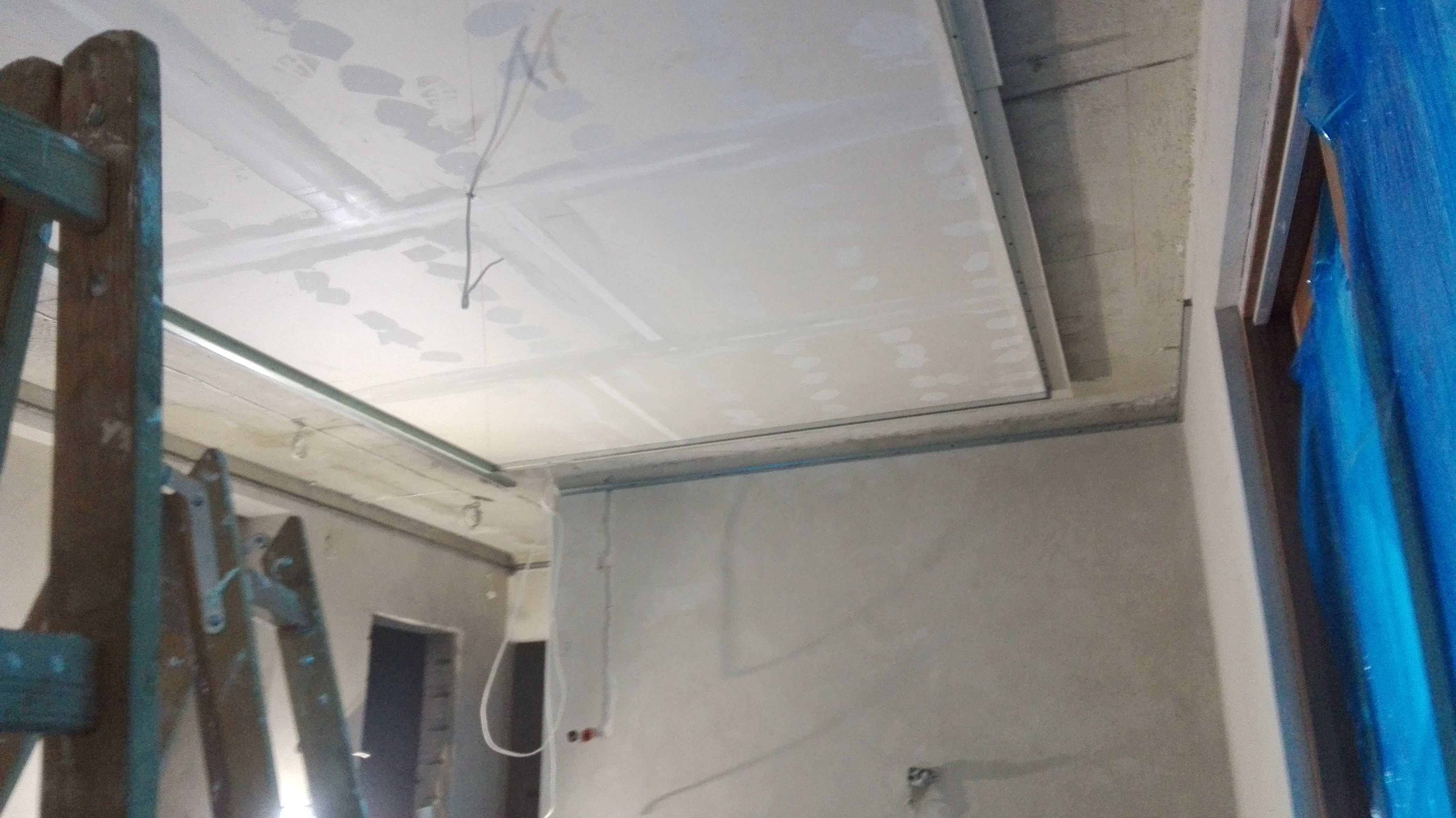 Montaż sufitu podwieszanego z płyt gipsowo-kartonowych, widoczne profile i instalacja elektryczna, drabina malarska z boku.