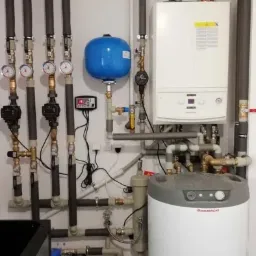 Złożona instalacja grzewcza w kotłowni z piecem gazowym Immergas, zasobnikiem ciepłej wody, naczyniem przeponowym, rozdzielaczem z pompami obiegowymi i sterownikiem, rury zaizolowane.