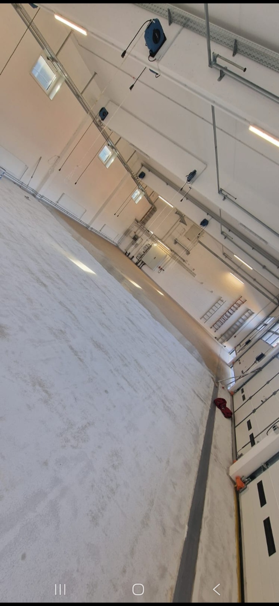 Wnętrze hali produkcyjnej po odświeżeniu: jasne ściany i podłoga, widoczne instalacje pod sufitem, drabiny przy ścianie. Ujęcie z dołu, podkreślające przestrzeń.