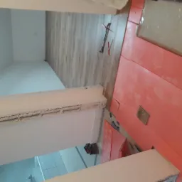 Widok z góry na przygotowanie podłoża pod panele: rozłożona izolacja w kolorze łososiowym i częściowo ułożone panele podłogowe o wzorze drewna, widoczne narzędzia.