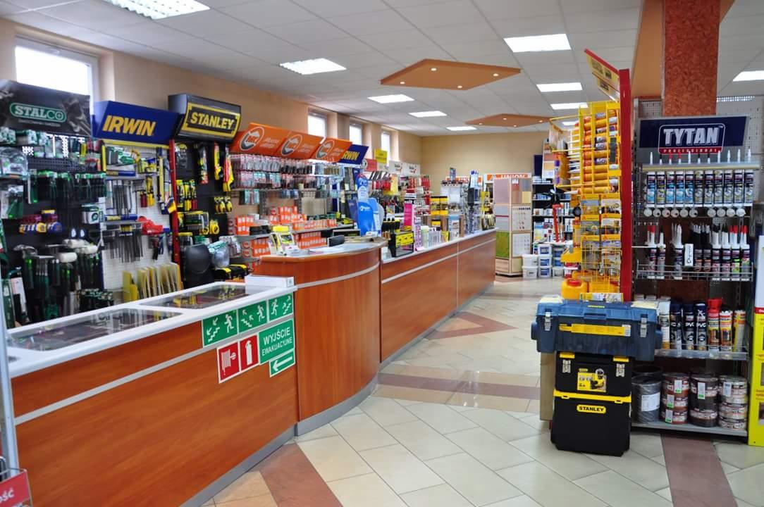 Wnętrze sklepu z narzędziami i materiałami budowlanymi, widok na kasę i regały z produktami marek Stalco, Irwin, Stanley i Tytan.