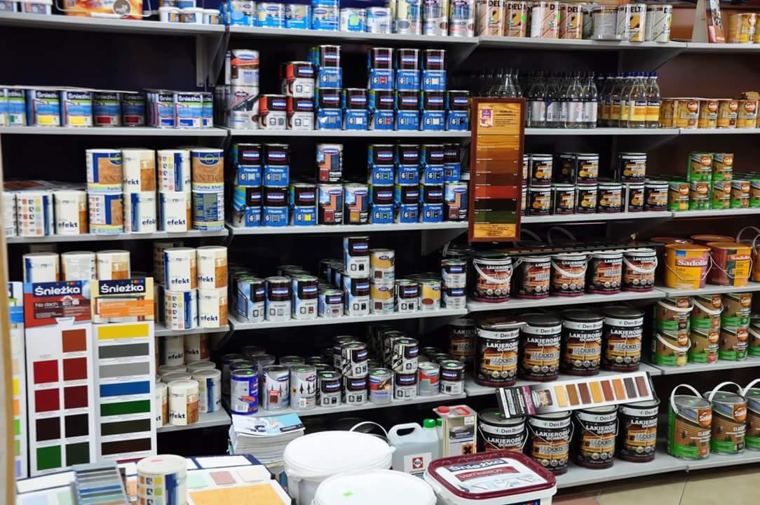 Półki w sklepie z farbami i lakierami, prezentujące różnorodność kolorów i marek, w tym Śnieżka i Lakierobójca, z ekspozycją próbek kolorystycznych na drewnianych panelach.