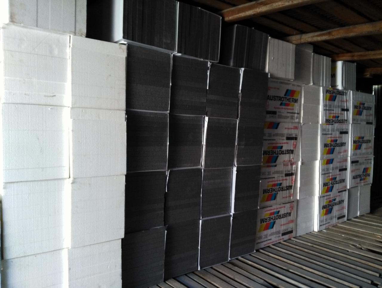 Skladowane płyty termoizolacyjne Austrotherm: białe, grafitowe i w opakowaniach foliowych, przygotowane do ocieplenia budynku.