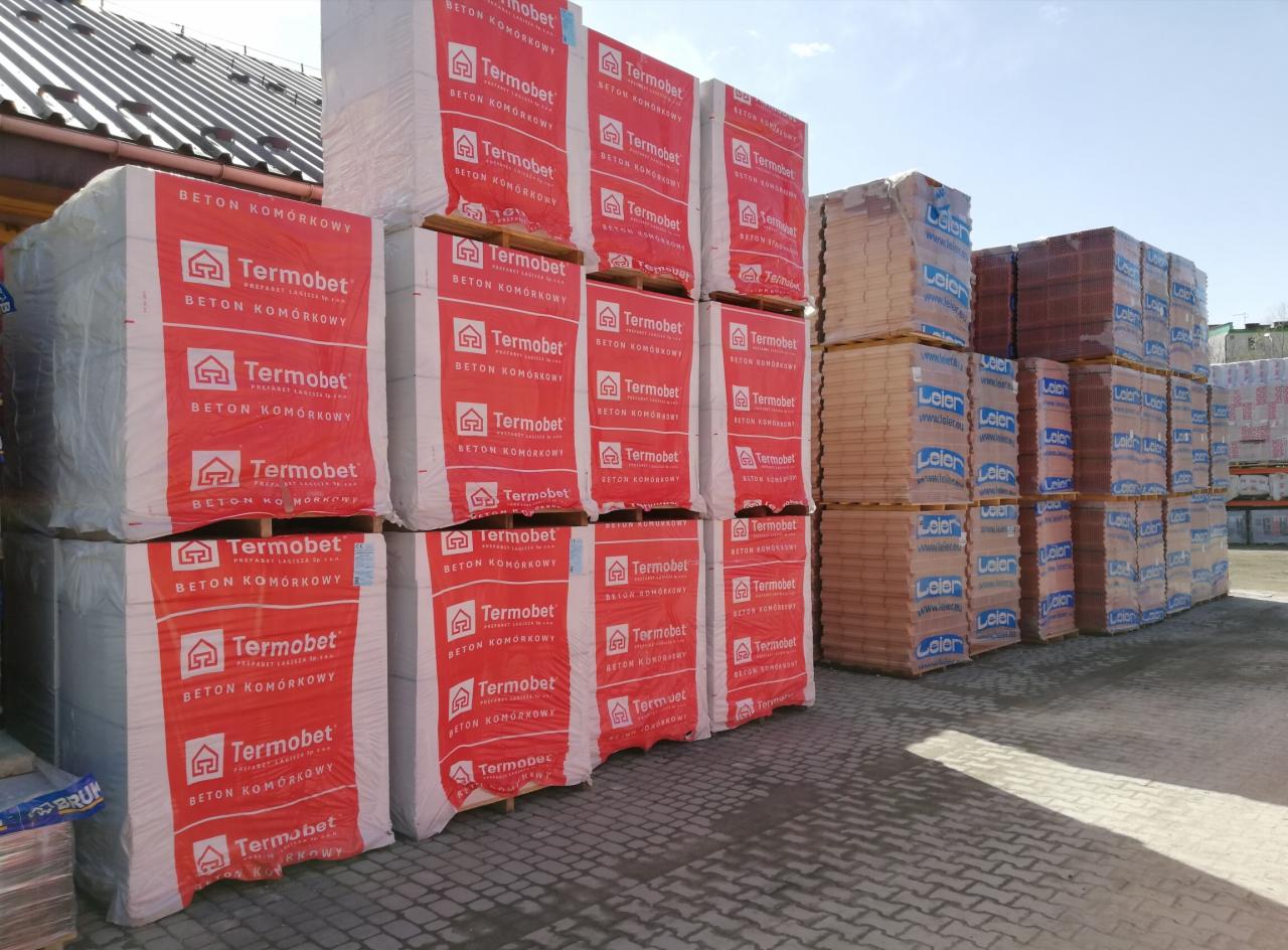 Palety z zapakowanymi bloczkami z betonu komórkowego Termobet na placu budowy, widoczne również cegły Leier.