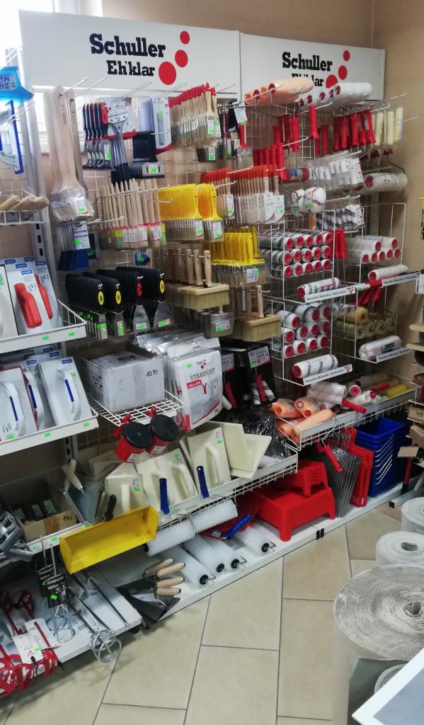 Półki w sklepie z narzędziami malarskimi i akcesoriami do wykończenia ścian, widoczne wałki, pędzle, szpachelki, kuwety i inne akcesoria marki Schuller Eh'klar.
