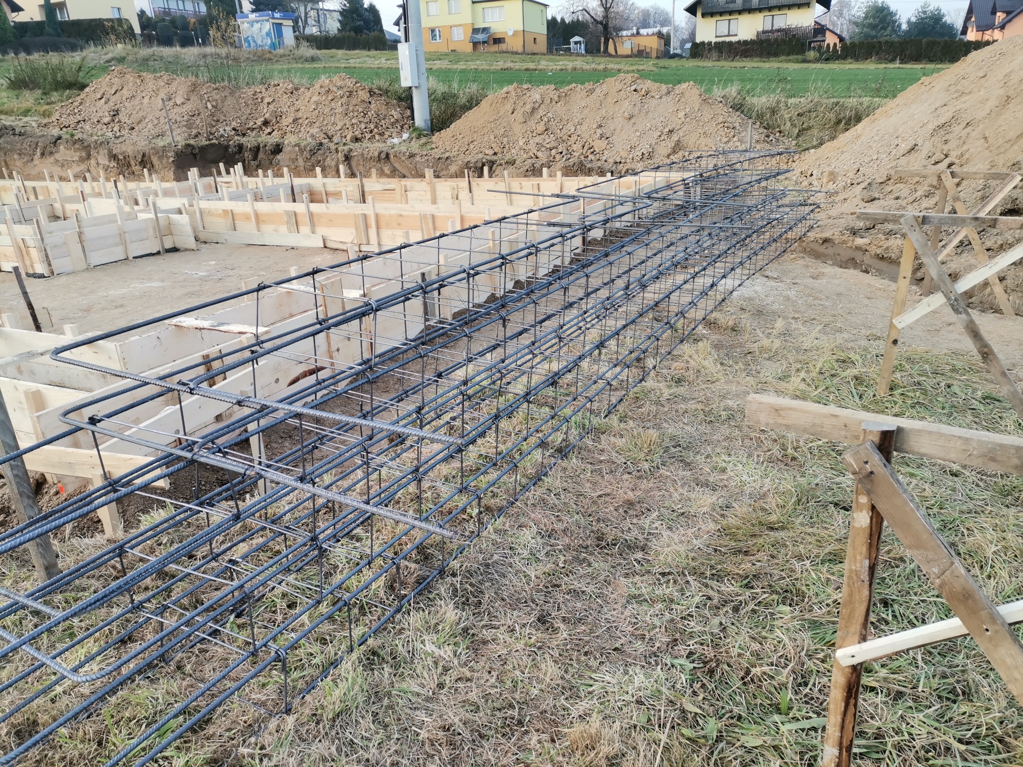 Zbrojenie fundamentów w wykopie, szalunki drewniane, pryzmy ziemi w tle