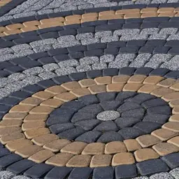 Wzór koncentrycznych okręgów ułożony z kostki brukowej w odcieniach szarości, grafitu i beżu, tworzący dekoracyjny element nawierzchni.