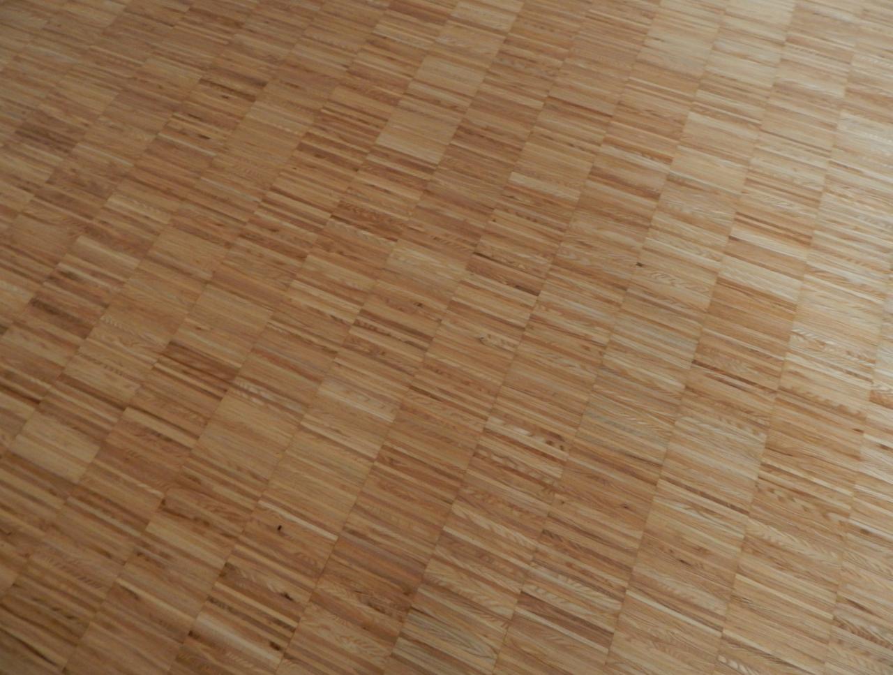 Parkiet ułożony w jodełkę, z wyraźnie widocznym usłojeniem drewna i subtelnymi różnicami w odcieniach poszczególnych klepek.