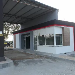 Nowoczesny budynek z oknami i automatycznymi drzwiami wejściowymi, wykończony w kolorach szarości, bieli i czerni z czerwoną linią akcentującą, w trakcie prac wykończeniowych na zewnątrz.