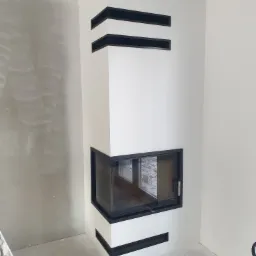 Nowoczesny narożny kominek z czarnymi akcentami w trakcie wykończenia, ściana po lewej stronie jeszcze nie wyszpachlowana.