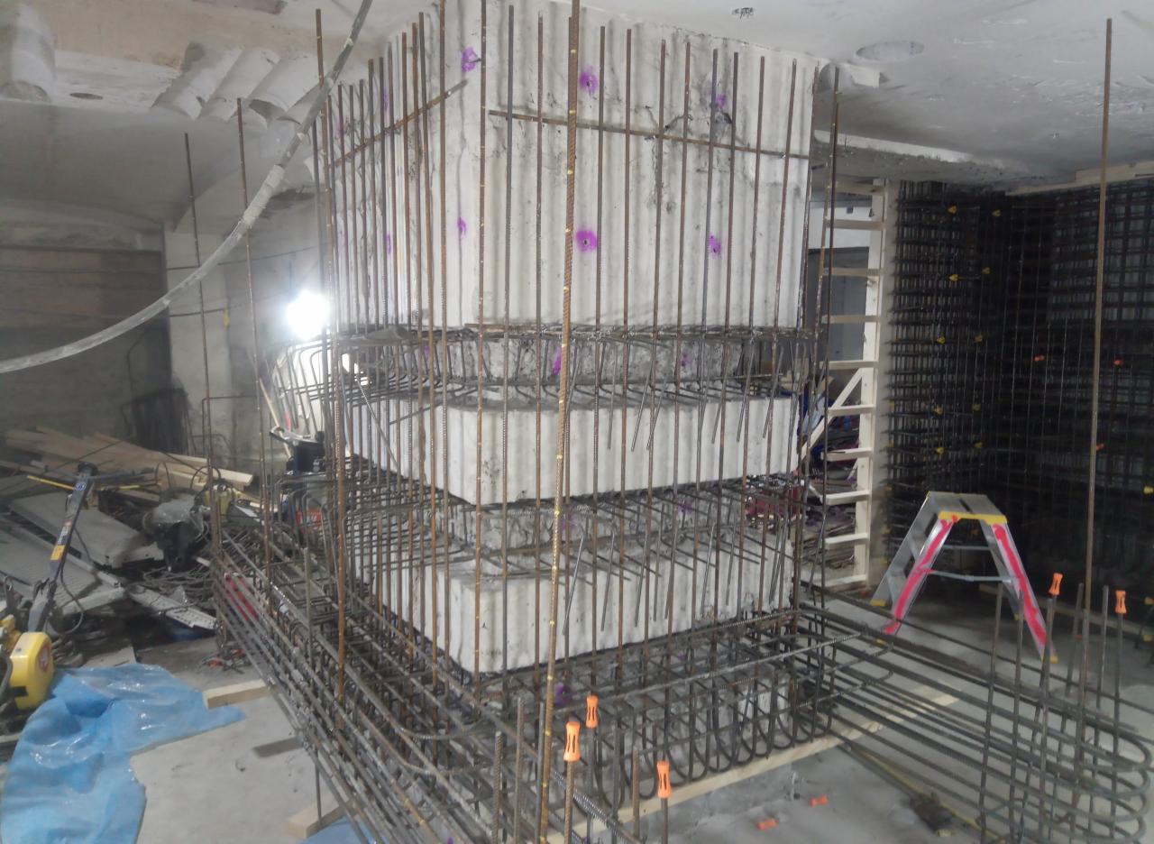 Wzmocniona stalą betonowa kolumna w trakcie budowy, widoczne szalunki i zbrojenie, praca w toku.