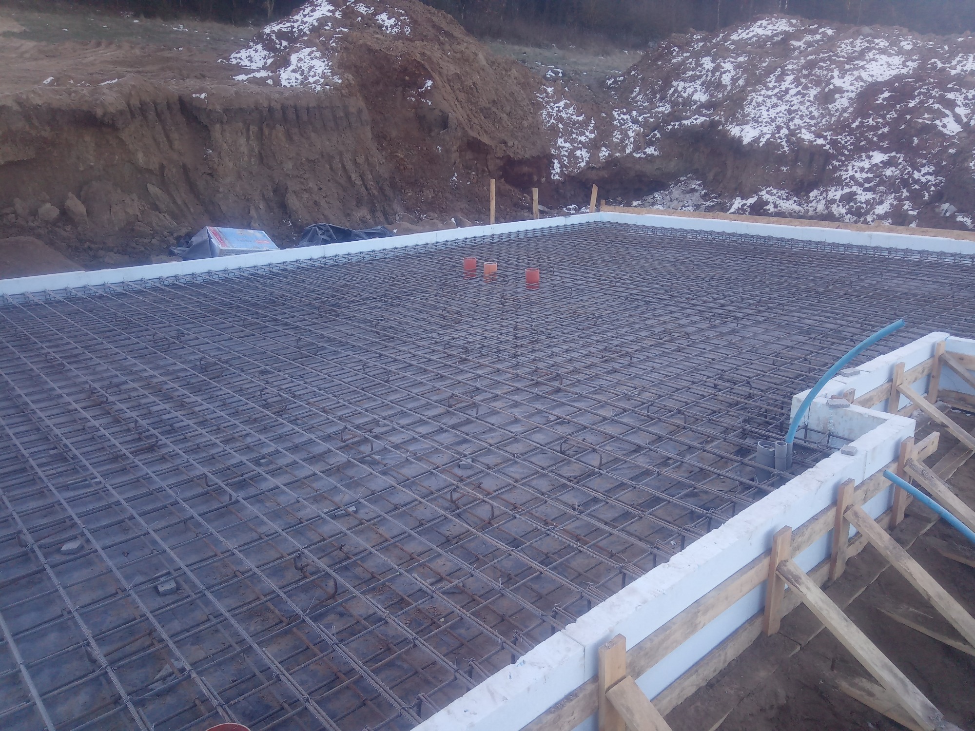 Siatka zbrojeniowa przygotowana do zalania betonem, widoczne szalunki z izolacją termiczną, w tle wykop ziemny z resztkami śniegu.