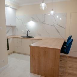 KWW Marcin Rzepniewski - Nowoczesna kuchnia w Kolnie z białymi szafkami, drewnianym blatem i marmurową ścianą, oświetlona wiszącymi lampami i uzupełniona o dwa niebieskie hokery.