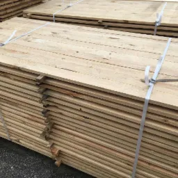 Stosy świeżo przetartego, jasnego drewna budowlanego, spięte białymi taśmami, ukazujące naturalny rysunek słojów i delikatne przebarwienia.