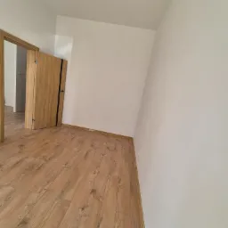 Jasne panele podłogowe w nowym pokoju z białymi ścianami i drewnianymi drzwiami z czarnym akcentem. Minimalistyczne wykończenie wnętrza.