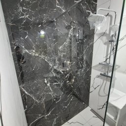 Remonty I Wykończenia Wnętrz Dominika Szczęsna - Elegancka kabina prysznicowa z czarnymi płytkami imitującymi marmur i białą armaturą. Nowoczesny design z widocznymi elementami chromowanymi.
