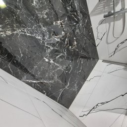 Remonty I Wykończenia Wnętrz Dominika Szczęsna - Nowoczesna łazienka z czarno-białymi płytkami imitującymi marmur ułożonymi pod kątem, widoczna armatura prysznicowa i odpływ liniowy.