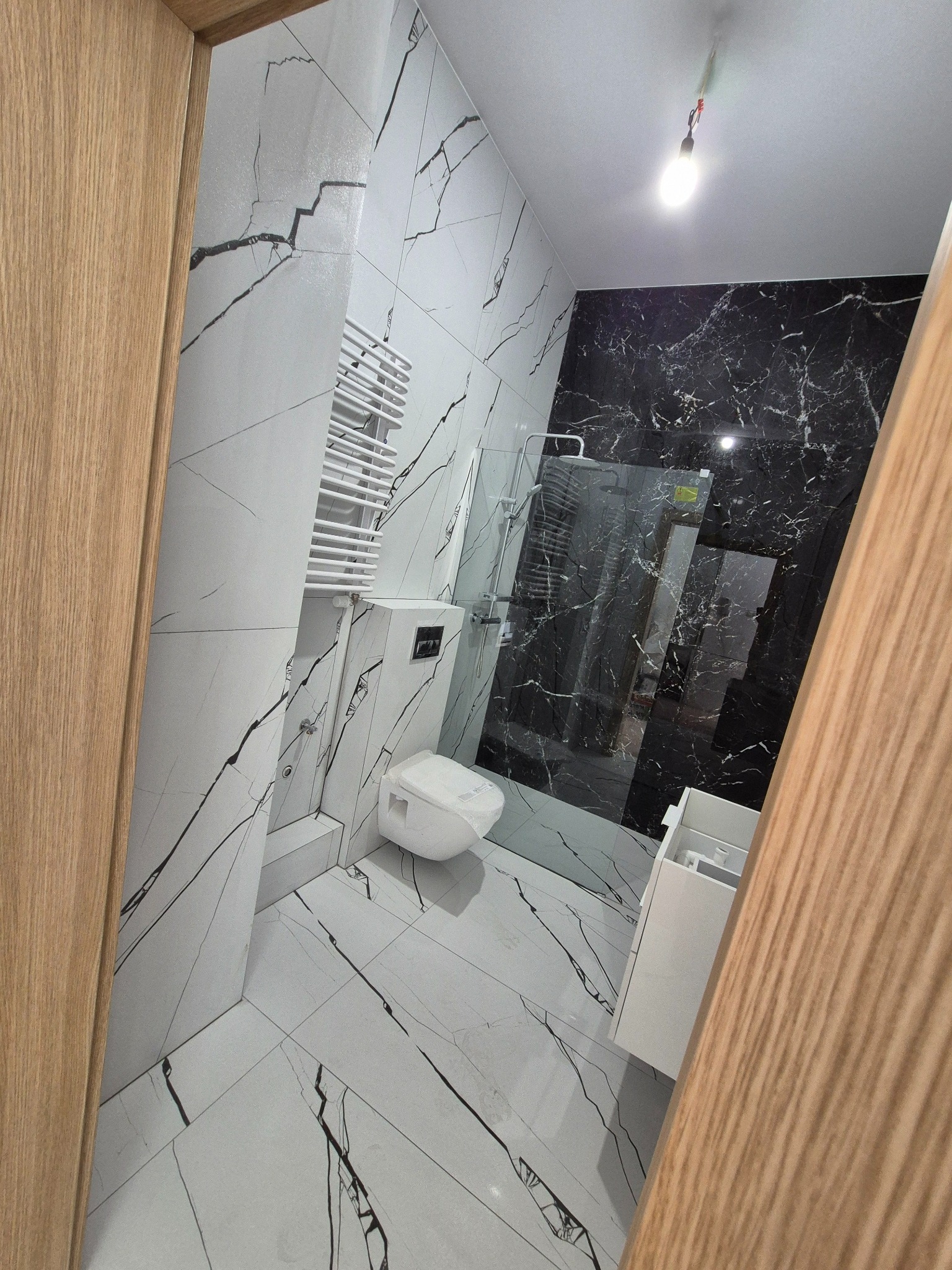 Nowoczesna łazienka z białymi i czarnymi płytkami imitującymi marmur, kabiną prysznicową typu walk-in i grzejnikiem drabinkowym.