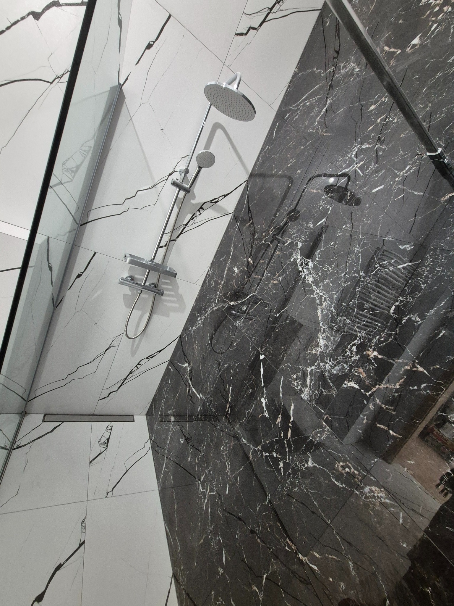 Nowoczesna kabina prysznicowa z marmurowymi płytkami w odcieniach bieli i czerni. Widoczna szklana ściana i chromowana armatura. Ujęcie z dołu, podkreślające detale wykończenia.