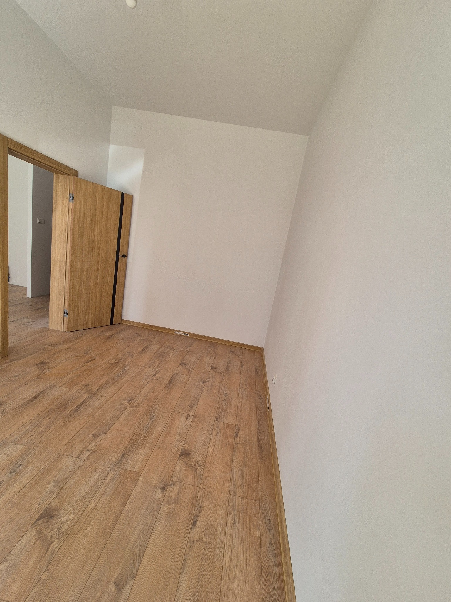 Jasne panele podłogowe w nowym pokoju z białymi ścianami i drewnianymi drzwiami z czarnym akcentem. Minimalistyczne wykończenie wnętrza.