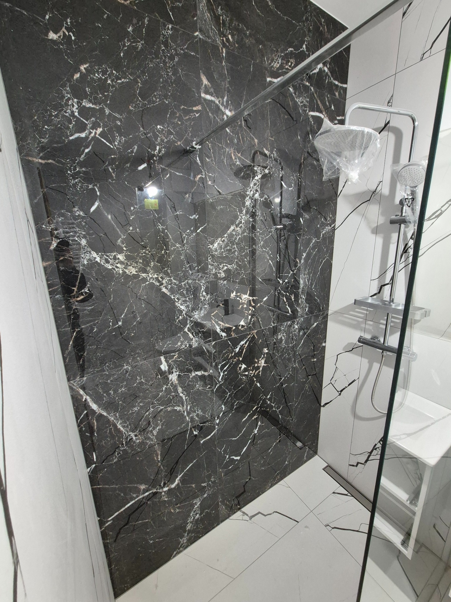 Elegancka kabina prysznicowa z czarnymi płytkami imitującymi marmur i białą armaturą. Nowoczesny design z widocznymi elementami chromowanymi.