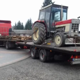 Czerwony ciągnik rolniczy Case 745 H z kabiną, przewożony na niskopodwoziowej przyczepie załadowanej drewnem, ciągniętej przez czerwony samoch&oacute;d ciężarowy