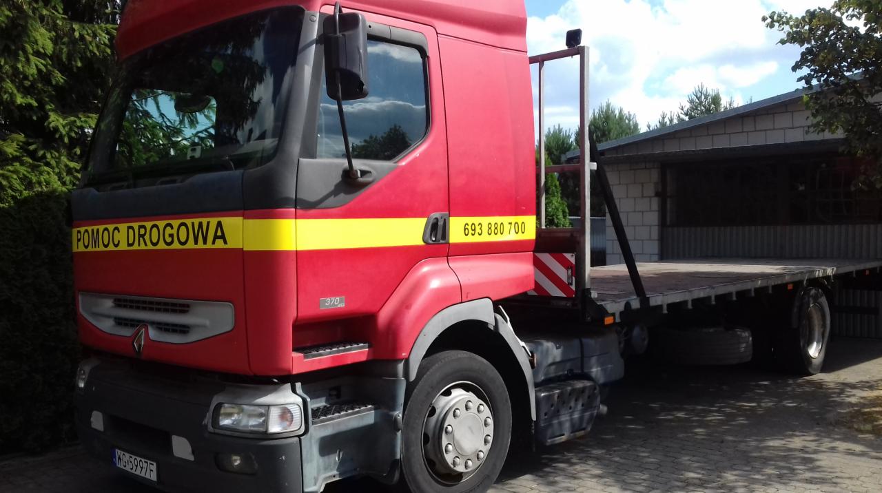 Czerwona ciężarówka pomocy drogowej z platformą w Garwolinie, z widocznym numerem telefonu na kabinie i tablicą rejestracyjną, zaparkowana przed budynkiem w słoneczny dzień.