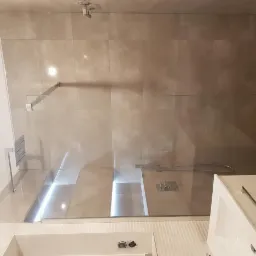 Nowoczesna kabina prysznicowa walk-in z szarymi płytkami imitującymi beton, chromowaną armaturą i odpływem liniowym w podłodze.