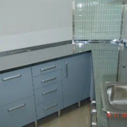 Fragment kuchni z niebieskimi szafkami z metalowymi uchwytami, blat ze stali nierdzewnej, zlewozmywak i płytki w odcieniach bieli i zieleni, sfotografowany w 2009 roku.