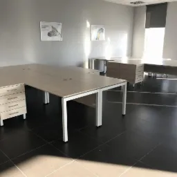 Jasne, minimalistyczne biurka z szufladami i białymi nogami w przestronnym biurze z czarną podłogą i plakatami na ścianach.