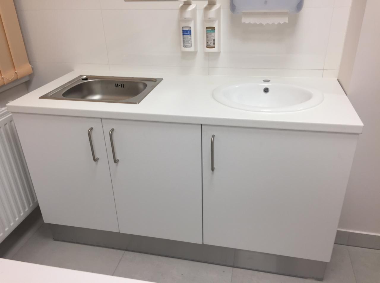 Biała szafka podumywalkowa z dwiema umywalkami (stalowa i ceramiczna) w łazience z dozownikami mydła na ścianie.