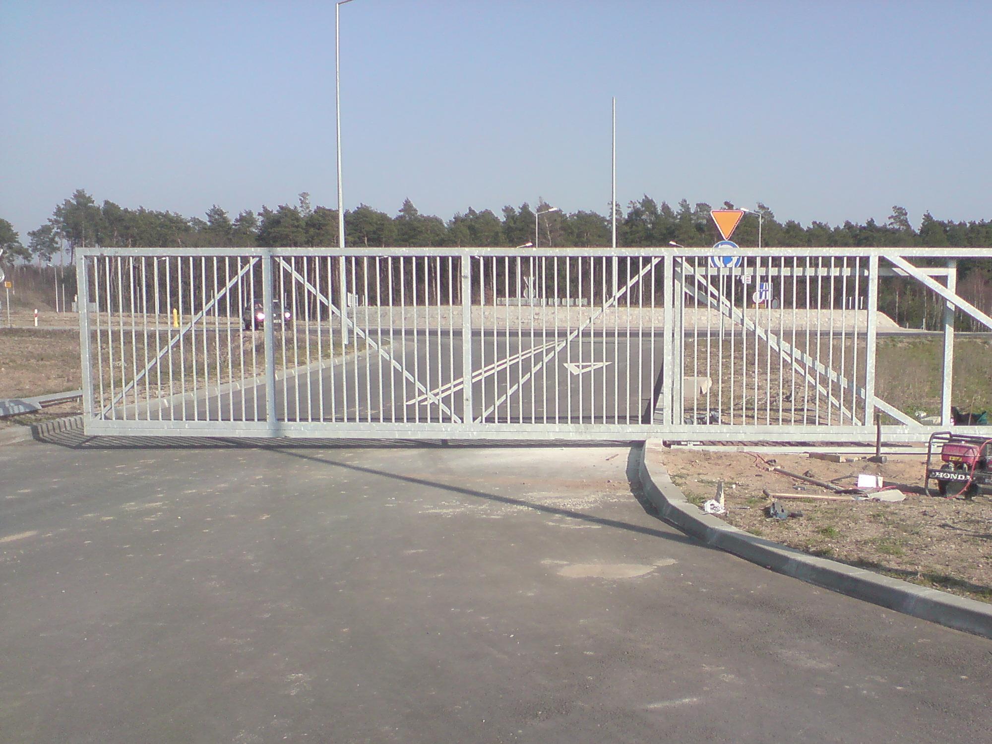 Przesuwna brama wjazdowa z metalowych prętów w trakcie montażu, widoczne narzędzia i agregat prądotwórczy Honda obok, w tle droga i las.