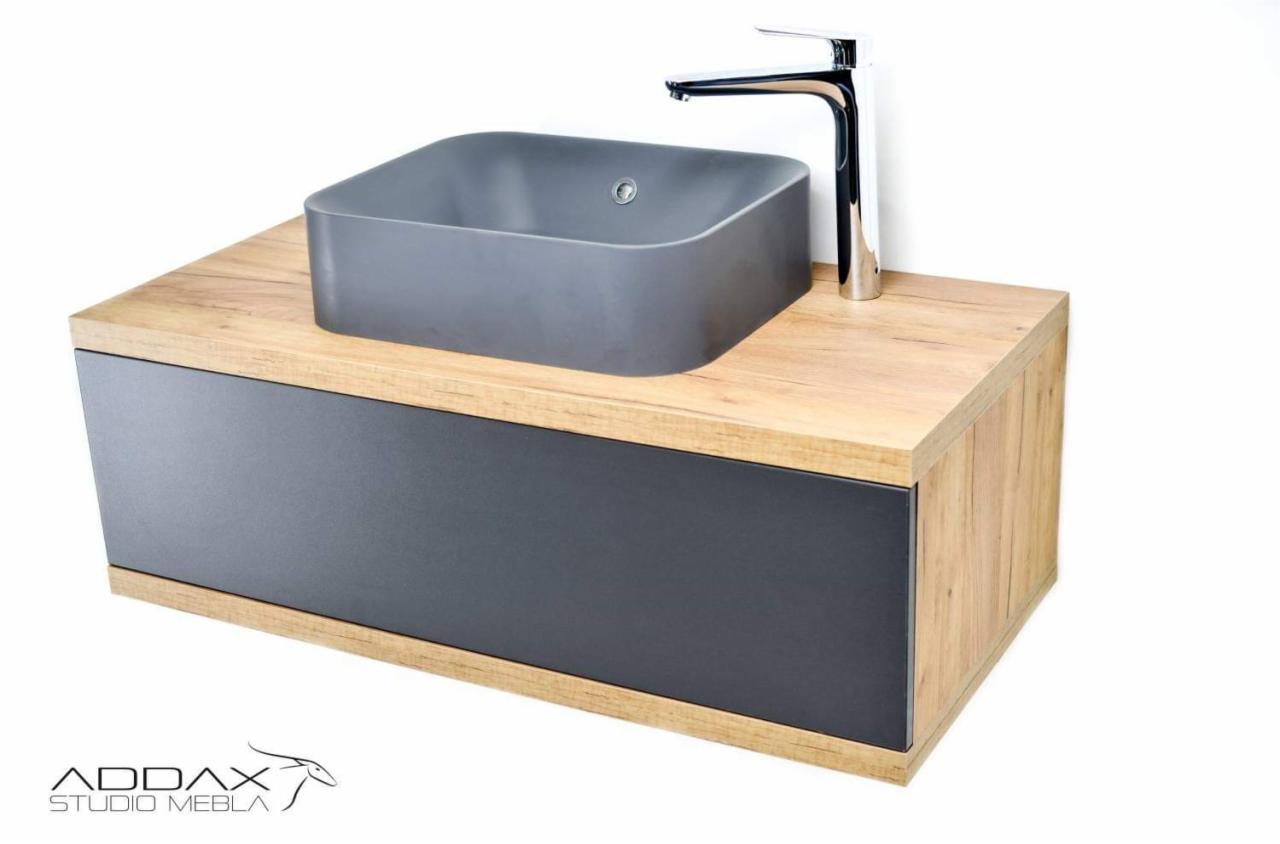 Szafka łazienkowa na wymiar z drewnianym blatem i szarą umywalką nablatową oraz chromowaną baterią, widoczne logo producenta ADDax Studio Mebla.