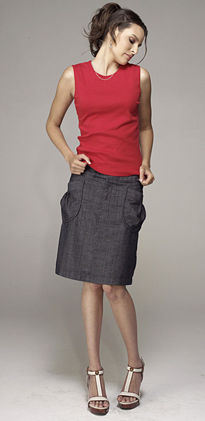 Kobieta prezentuje zestaw: czerwony top bez rękawów i szarą spódnicę z kieszeniami, uzupełniony sandałami na platformie z białymi paskami.