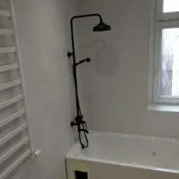 Biała wanna z czarną armaturą natryskową, widok na okno w łazience w Poznaniu.