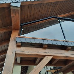 MARIUSZ SŁOMIŃSKI - Szklana balustrada na drewnianej konstrukcji balkonu z widocznym fragmentem dachu pokrytego łupkiem.