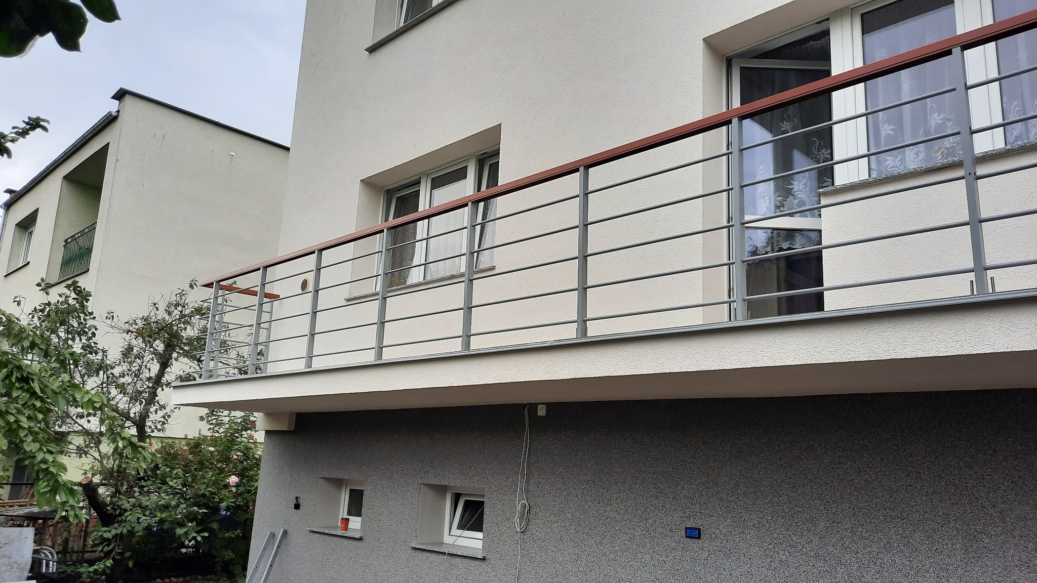 Balkon z balustradą ze stali nierdzewnej i drewnianą poręczą w nowoczesnym budynku mieszkalnym, widok z dołu, drabina oparta o ścianę.