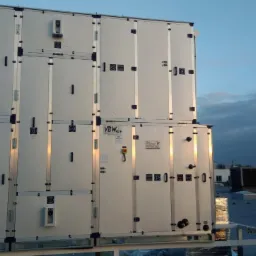 Złożona z segmentów centrala wentylacyjna VBW Clima na dachu budynku, widoczne liczne przyłącza, czujniki i elementy sterujące, w tle zabudowa miejska i pochmurne niebo.