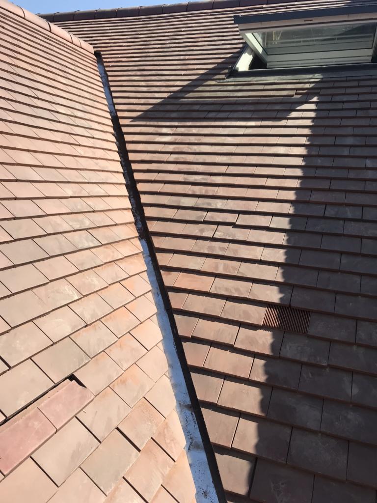 Czerwona dachówka ceramiczna ułożona na dachu z oknem dachowym, widoczny fragment kosza dachowego.