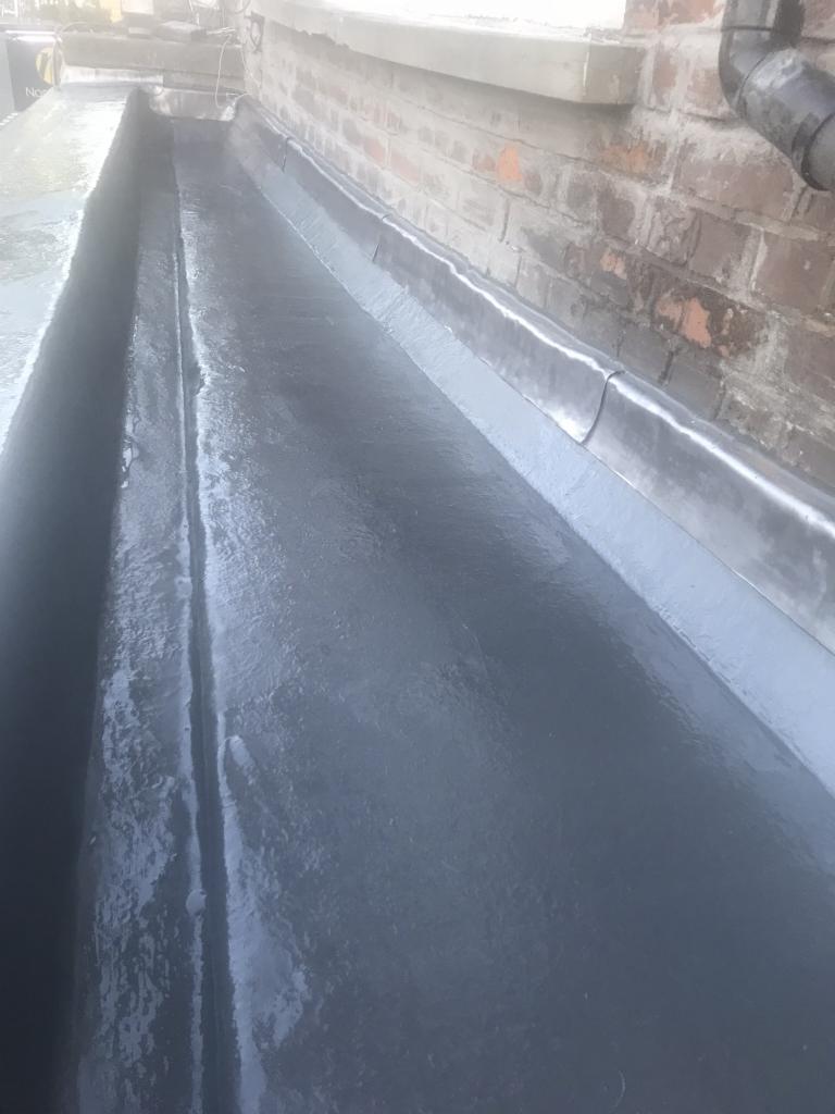 Szczelne połączenie blacharskie na dachu, widoczny fragment muru z cegły i rura spustowa.