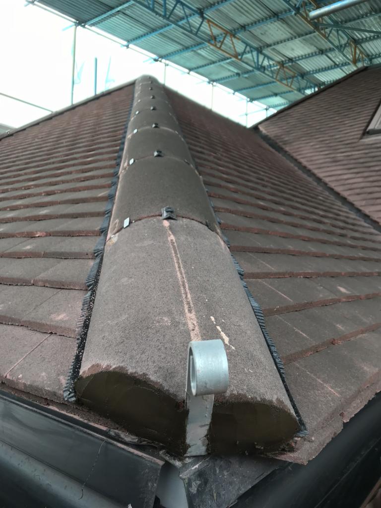 Kątowy widok na dach z brązową dachówką, zabezpieczony rusztowaniem, z widocznym systemem mocowania na kalenicy.