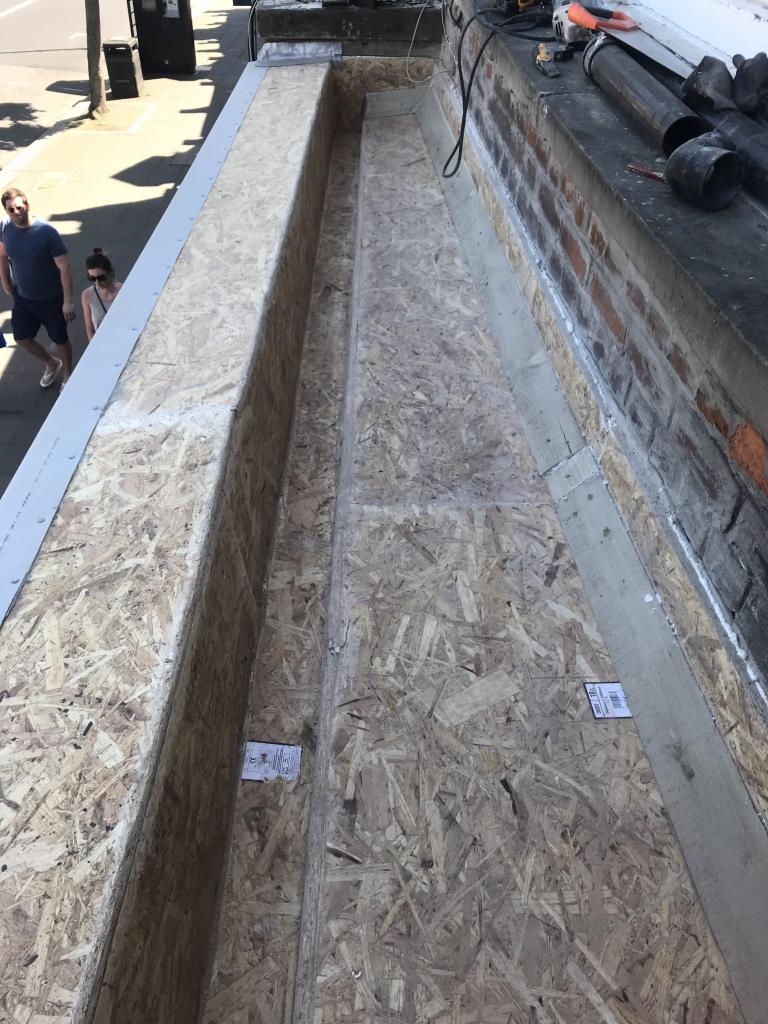 Konstrukcja dachu z desek OSB, widok z góry, z elementami muru i narzędziami w tle.